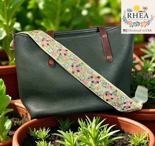 Green handbag with a floral strap in a garden setting, featuring the RHEA brand.