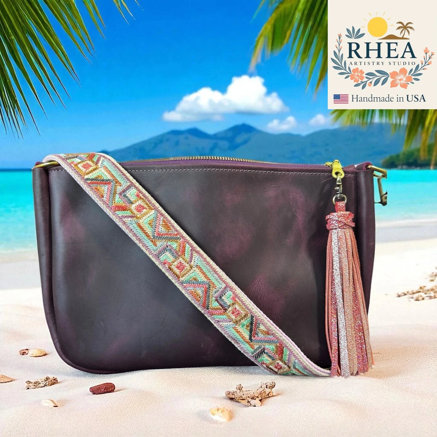 Brown leather handbag with colorful purse strap and tassel on a beach with palm trees and blue sky.