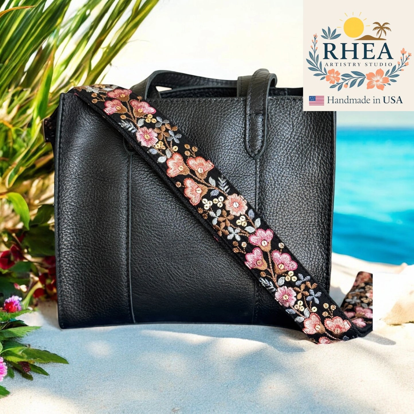 Black handbag with floral purse strap on a beach, featuring RHEA Artistry Studio logo.