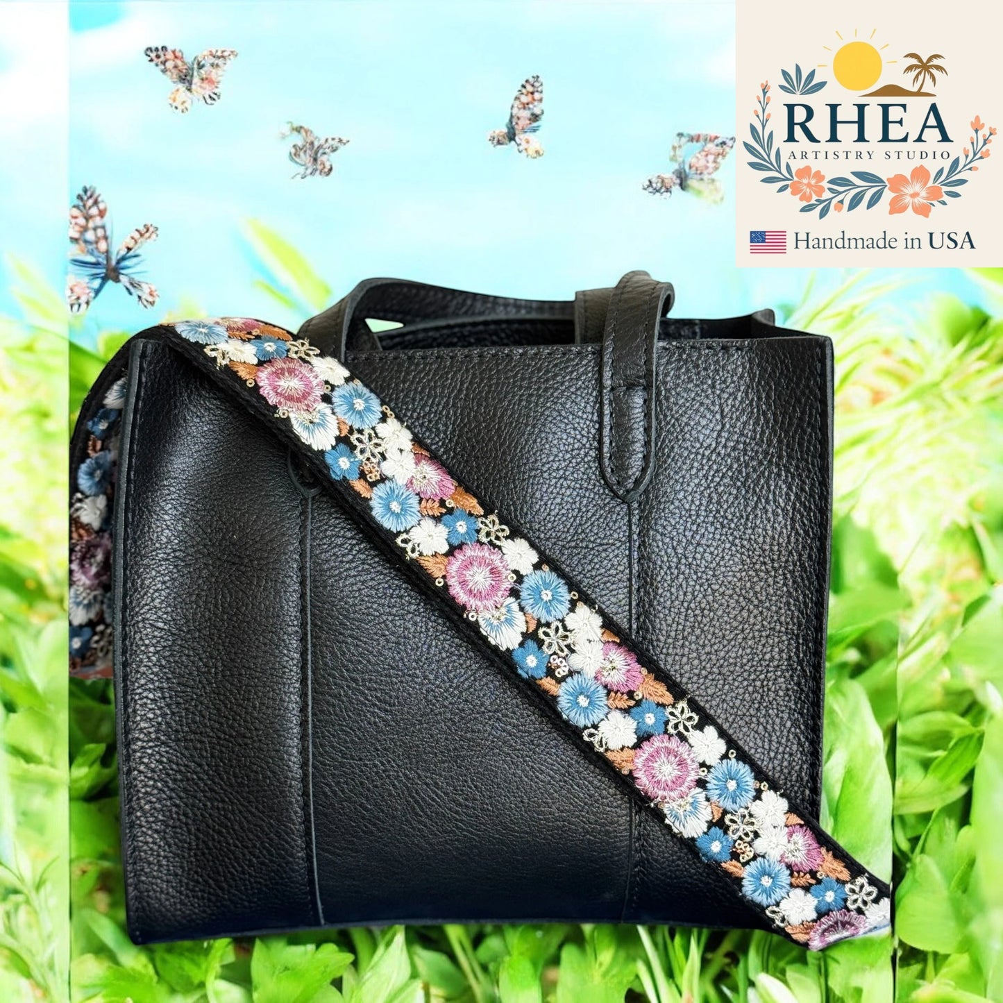 Black leather handbag with a colorful floral purse strap on a green background, featuring the Rhea Artistry Studio logo.