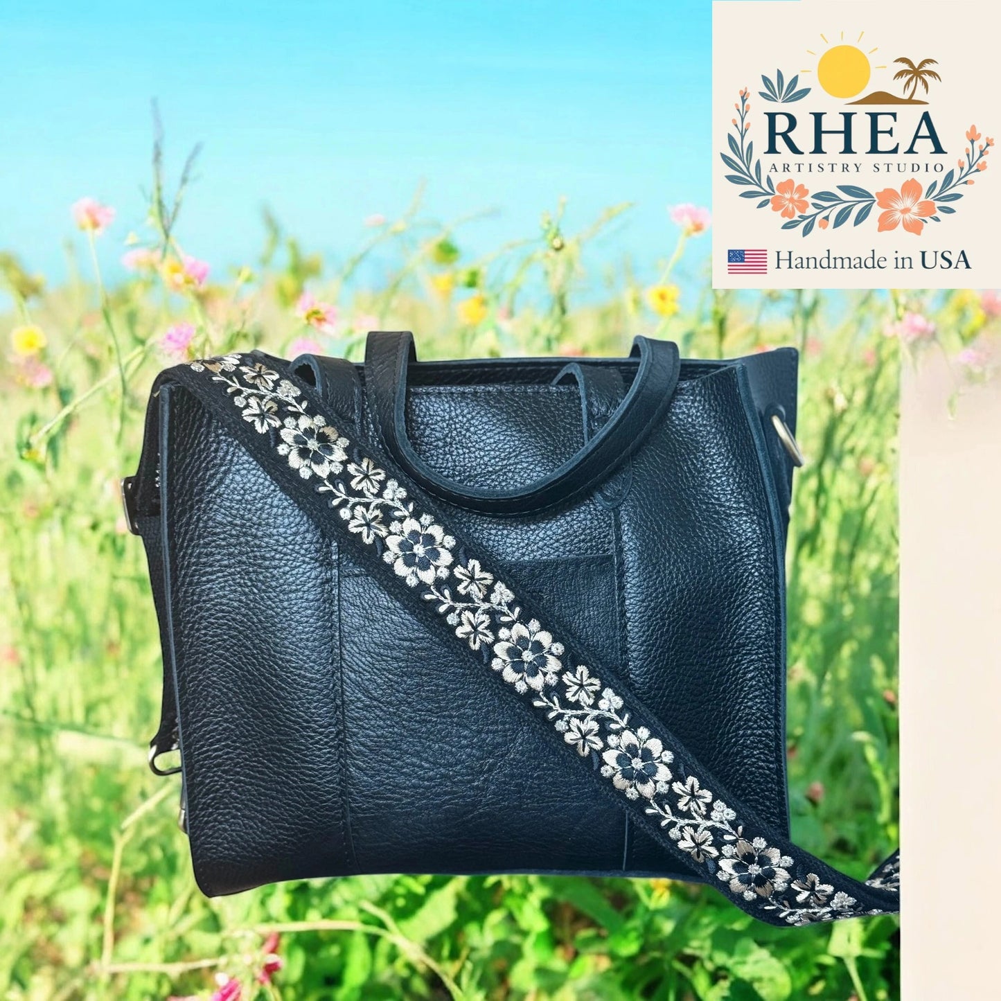 Black leather handbag with floral strap against a natural background, featuring the RHEA Artesian Studio logo.