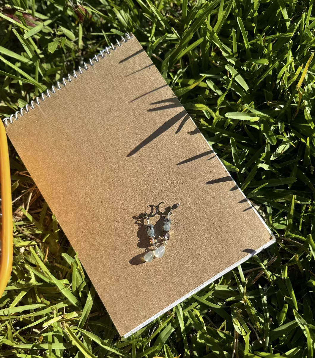 A pair of blue tulip silver earrings with a leverback closure, displayed on a brown notebook outdoors.