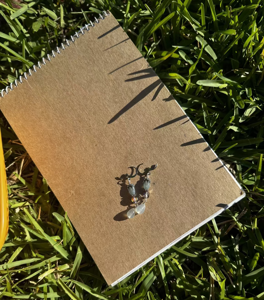 A pair of blue tulip silver earrings with a leverback closure, displayed on a brown notebook outdoors.