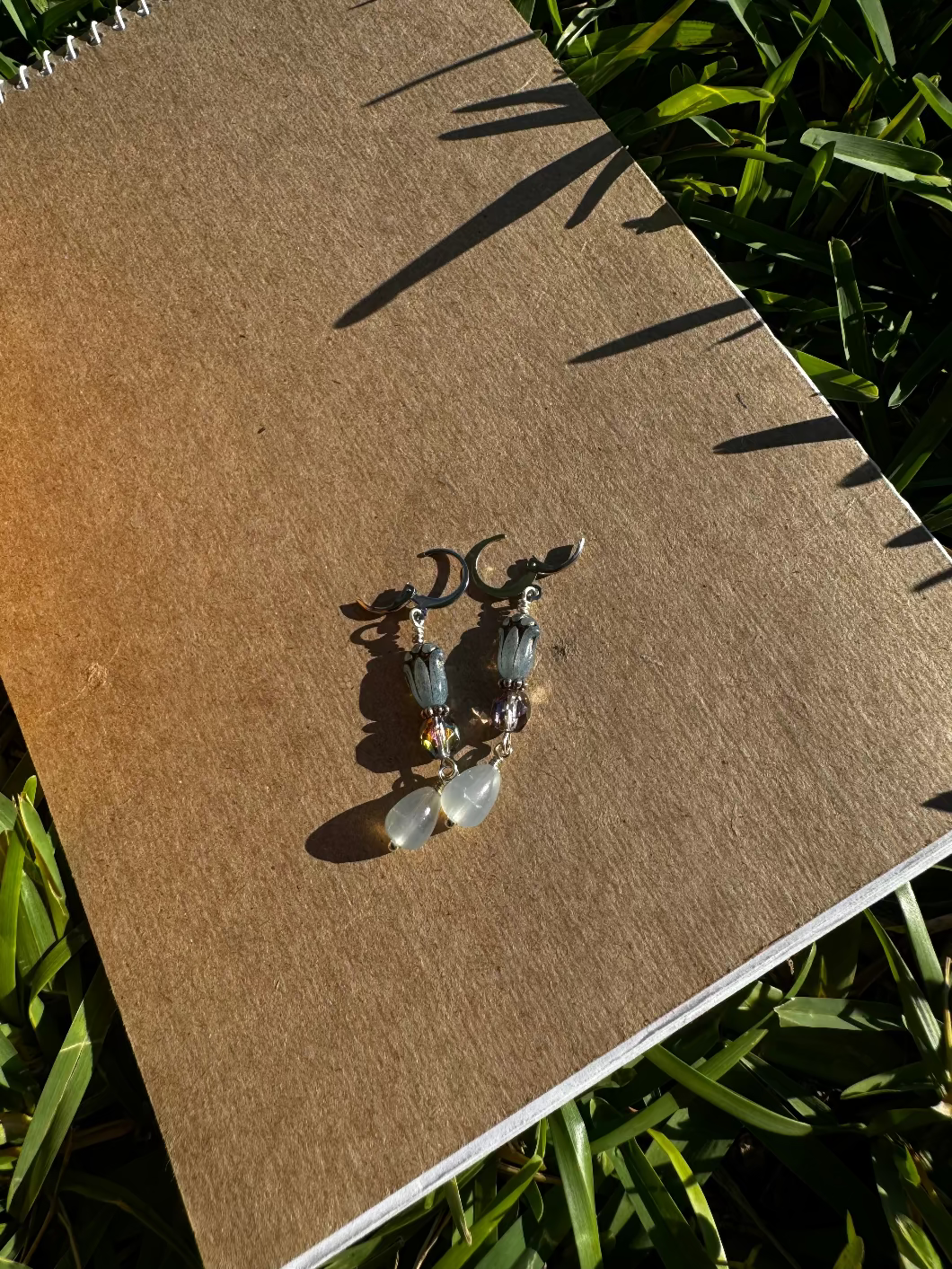 A pair of blue tulip silver earrings with a leverback closure, displayed on a brown notebook outdoors.