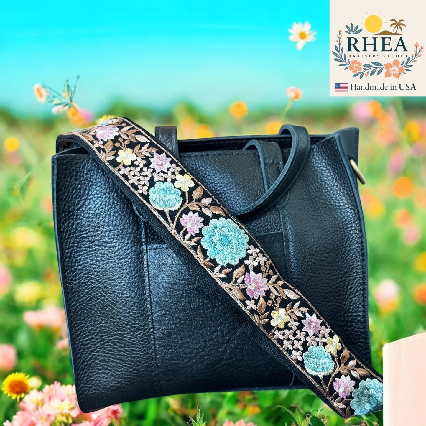 Black leather handbag with floral bag strap against a colorful floral background, featuring the RHEA brand.