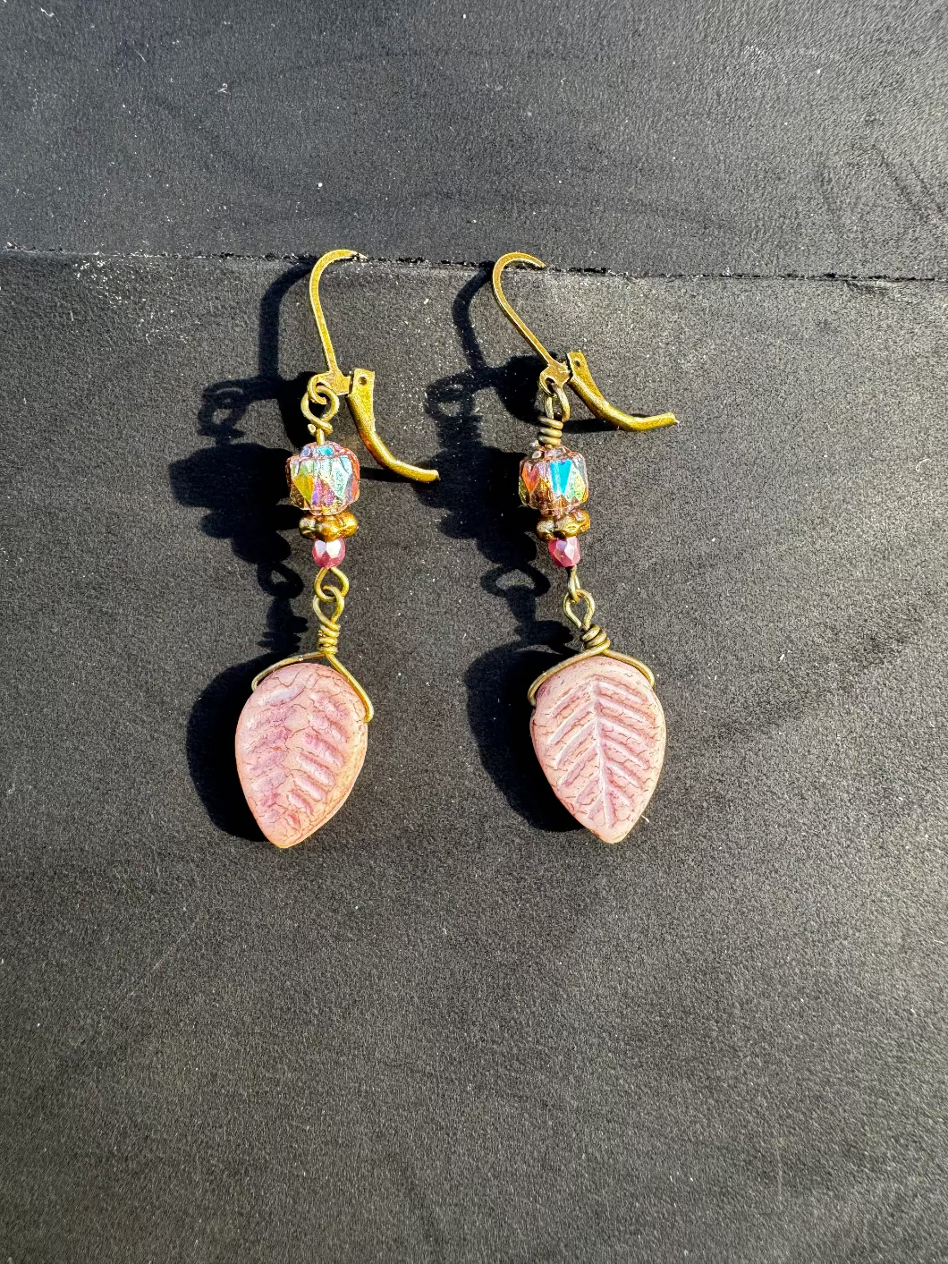 Handmade with Czech glass beads, these earrings have a celestial glow. They feature an antique bronze finish and brass hardware, including a leaf-shaped charm.
