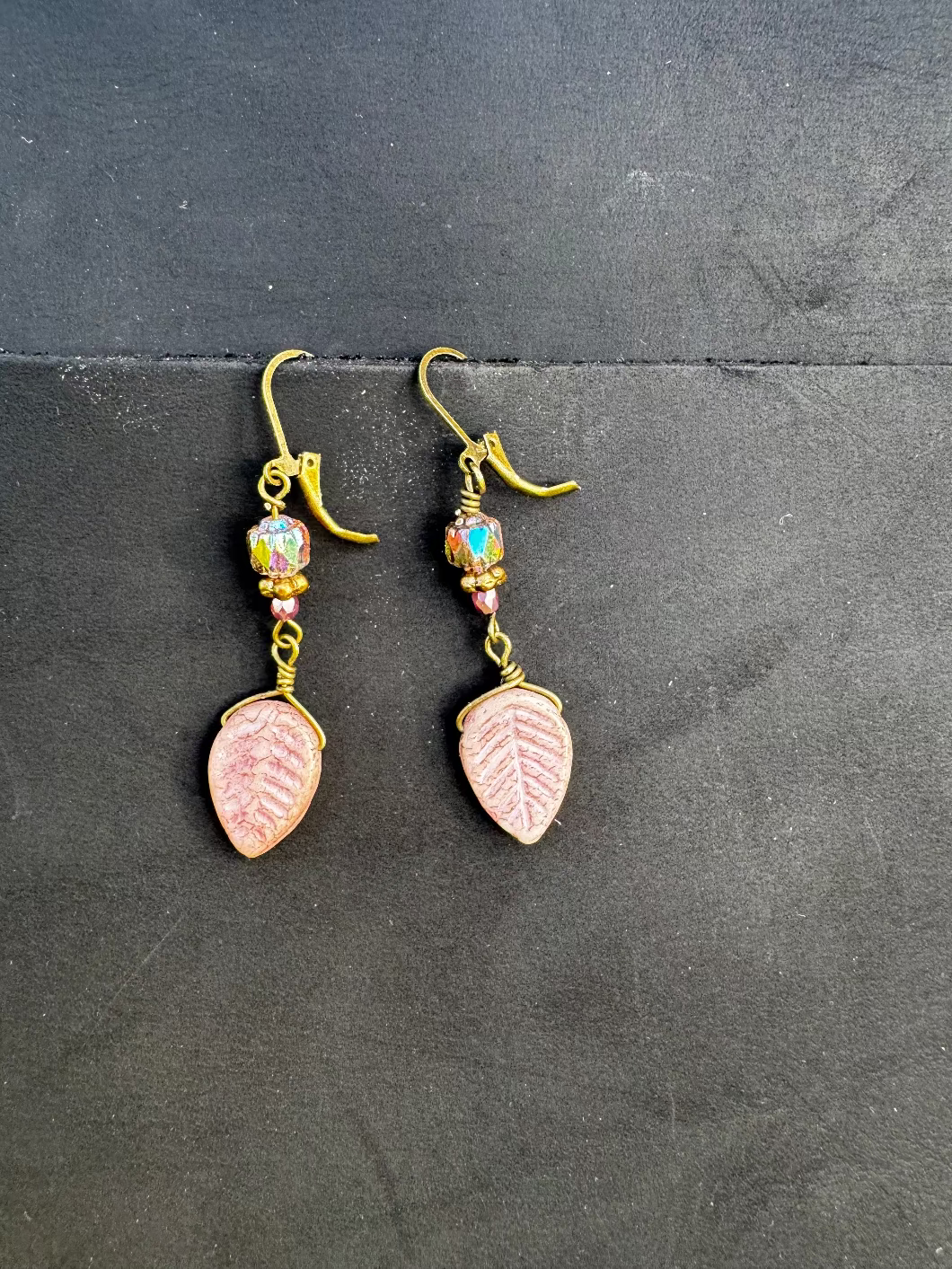 Handmade with Czech glass beads, these earrings have a celestial glow. They feature an antique bronze finish and brass hardware, including a leaf-shaped charm.