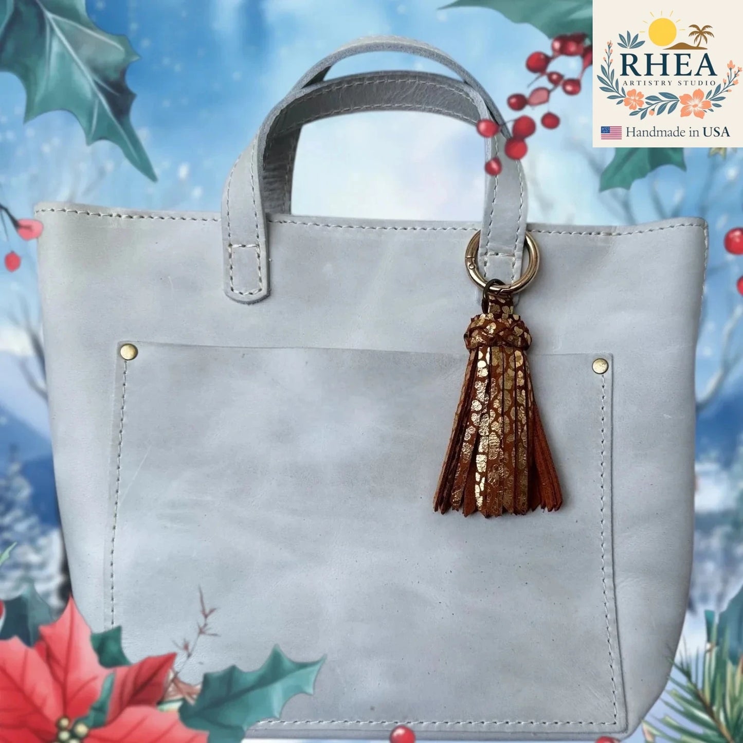 Gray handbag with a brown tassel keychain on a decorative background with holly leaves and berries.