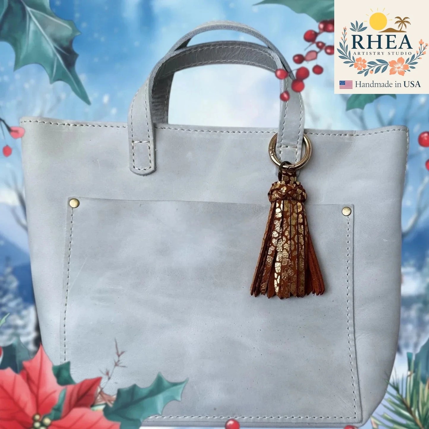Gray handbag with a gold tassel on a decorative background featuring holly leaves and berries.
