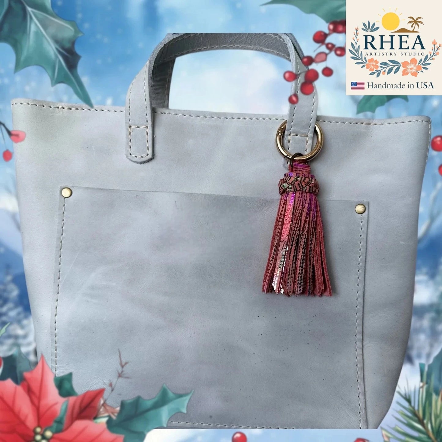 Gray handbag with a tassel on a decorative background featuring Christmas elements and the RHEA brand logo.