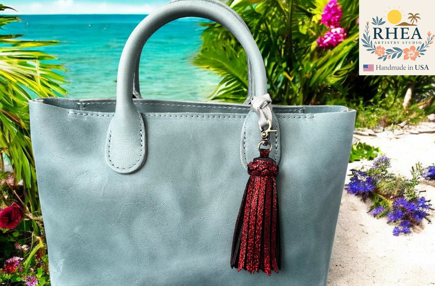 Light blue handbag with a red tassel on a beach background, featuring the RHEA brand.