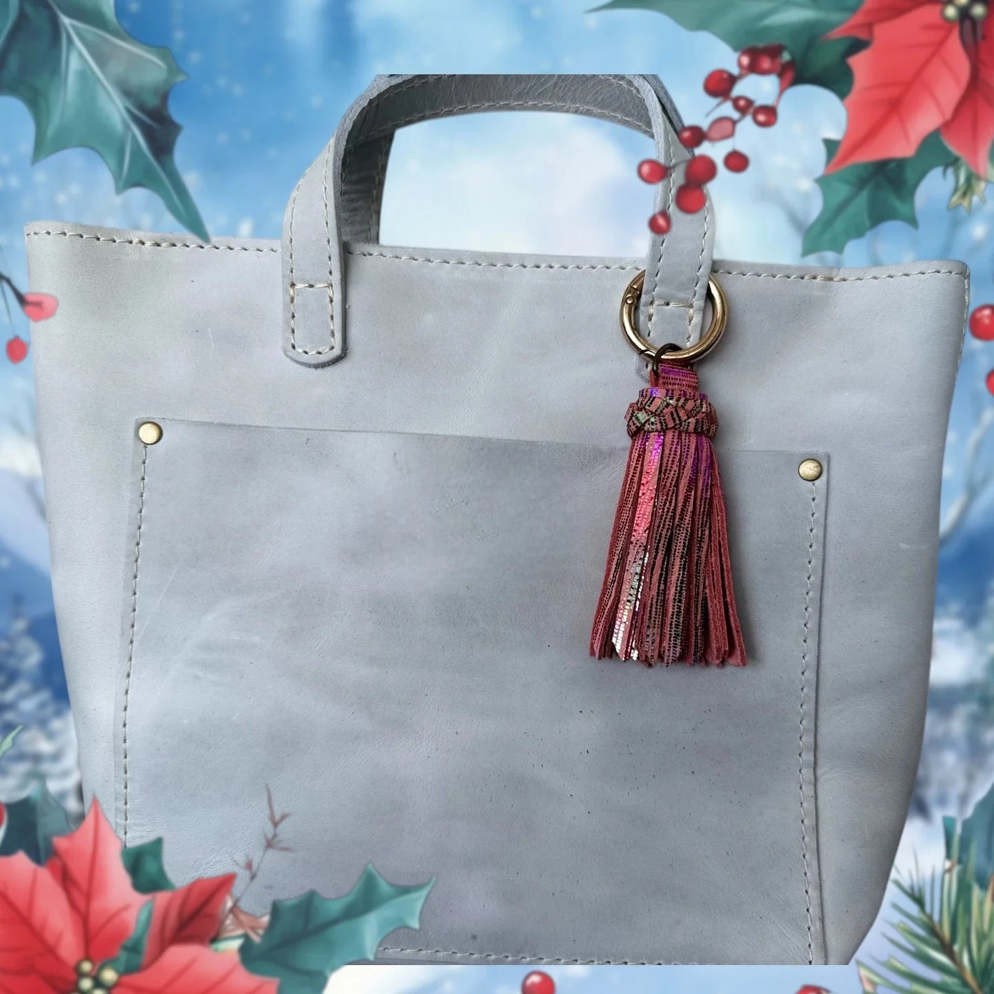 Gray handbag with a tassel detail on a decorative background with holly leaves and berries.