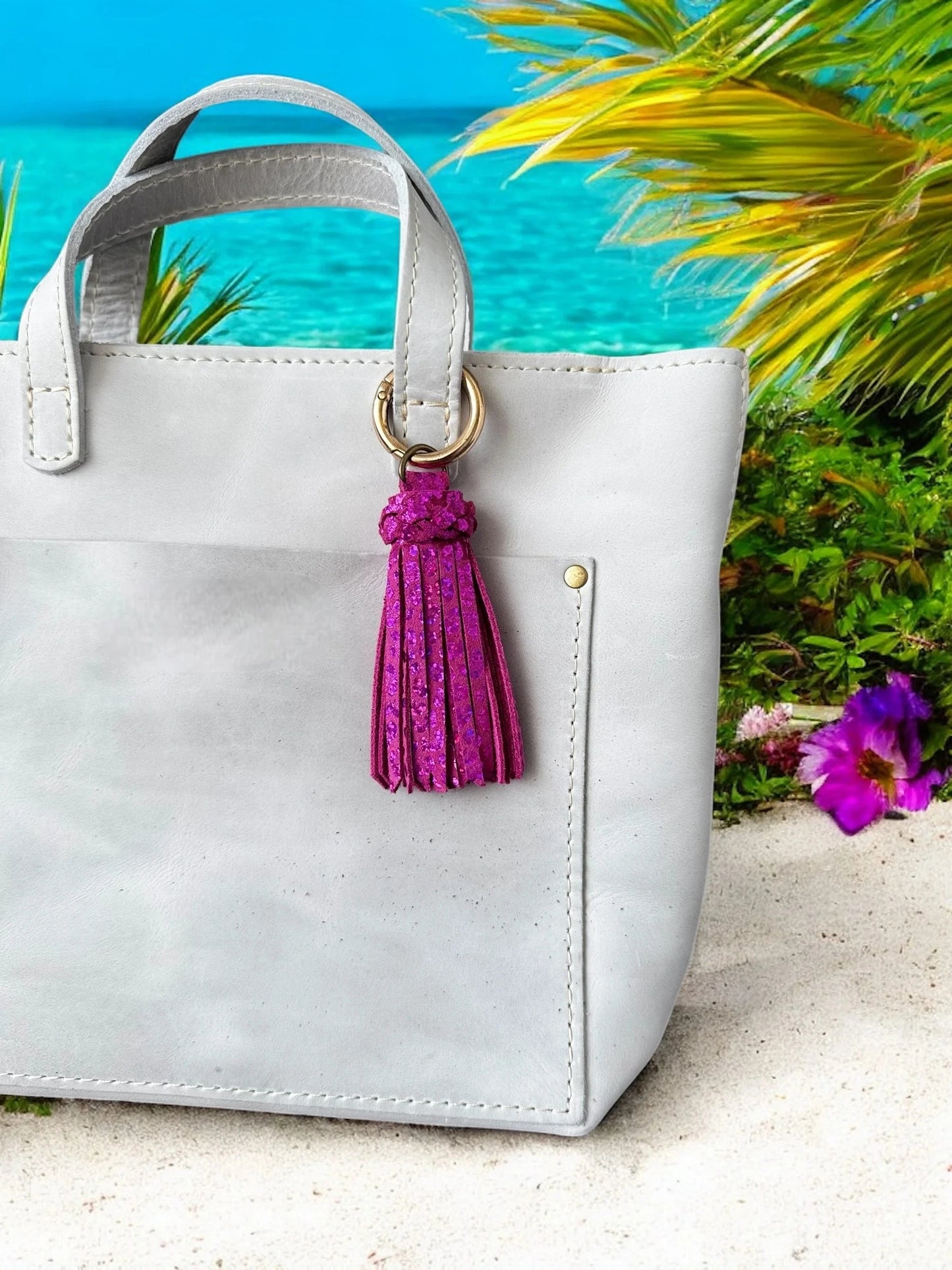 White handbag with a pink tassel on a sandy surface with a beach background