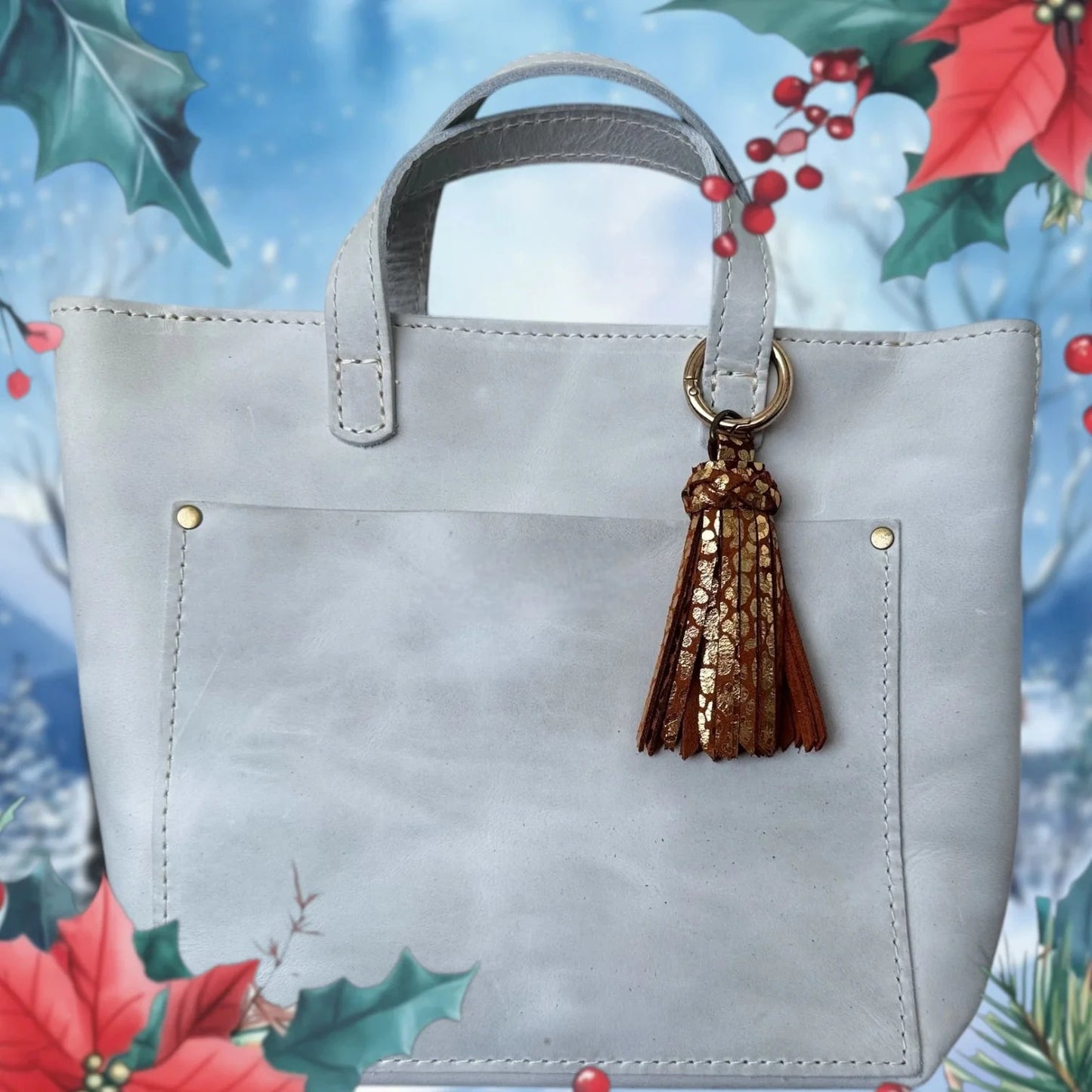 Gray handbag with a brown tassel on a decorative background with holly and berries.