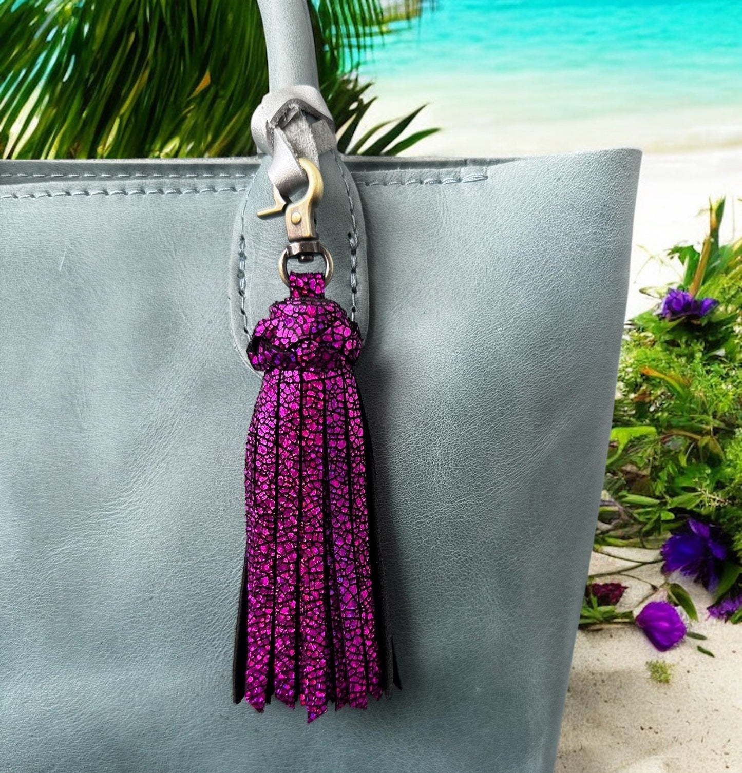 Purple tassel keychain attached to a gray handbag with a beach background