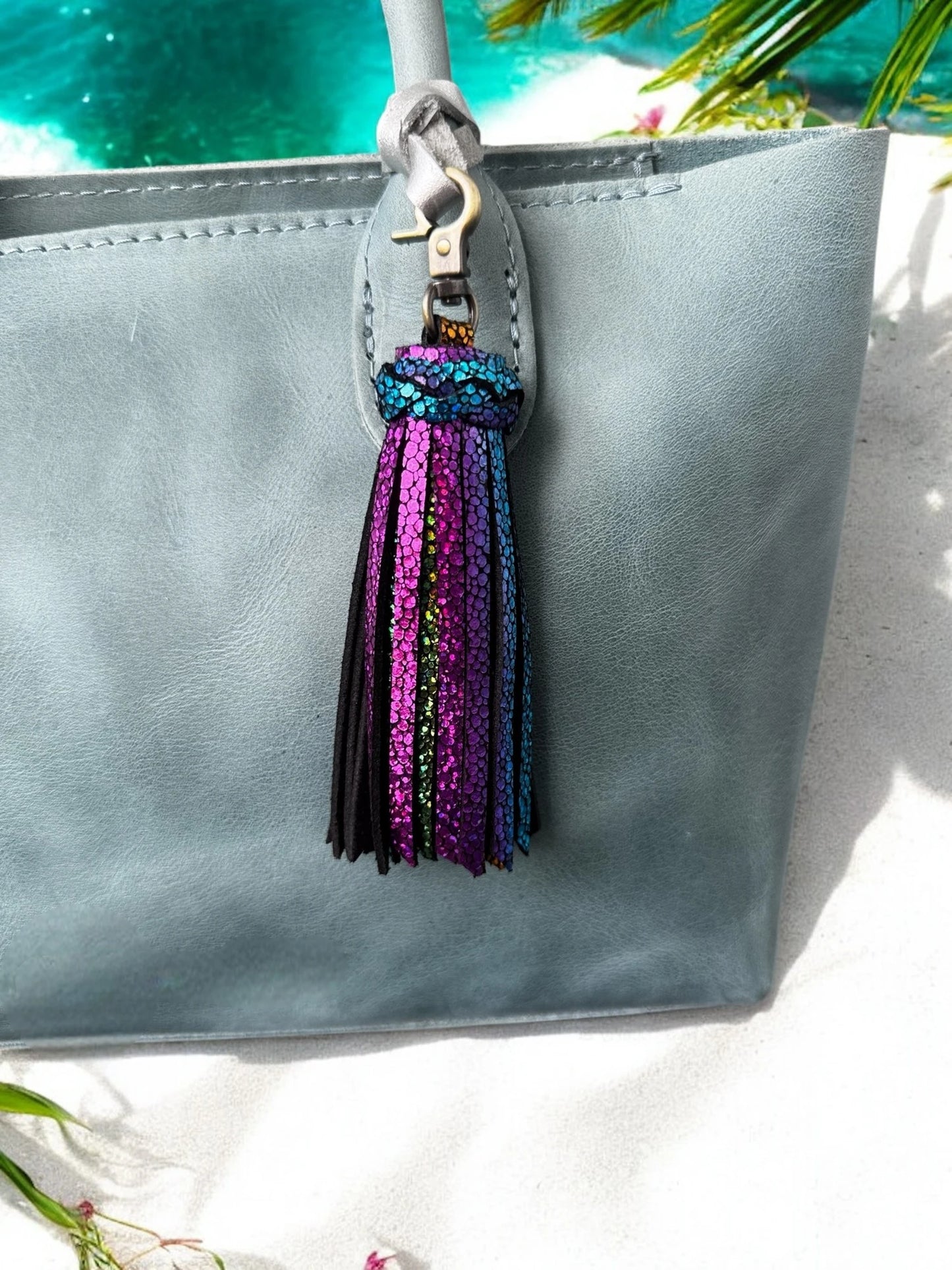 Gray clutch bag with a colorful tassel on a white surface with greenery.