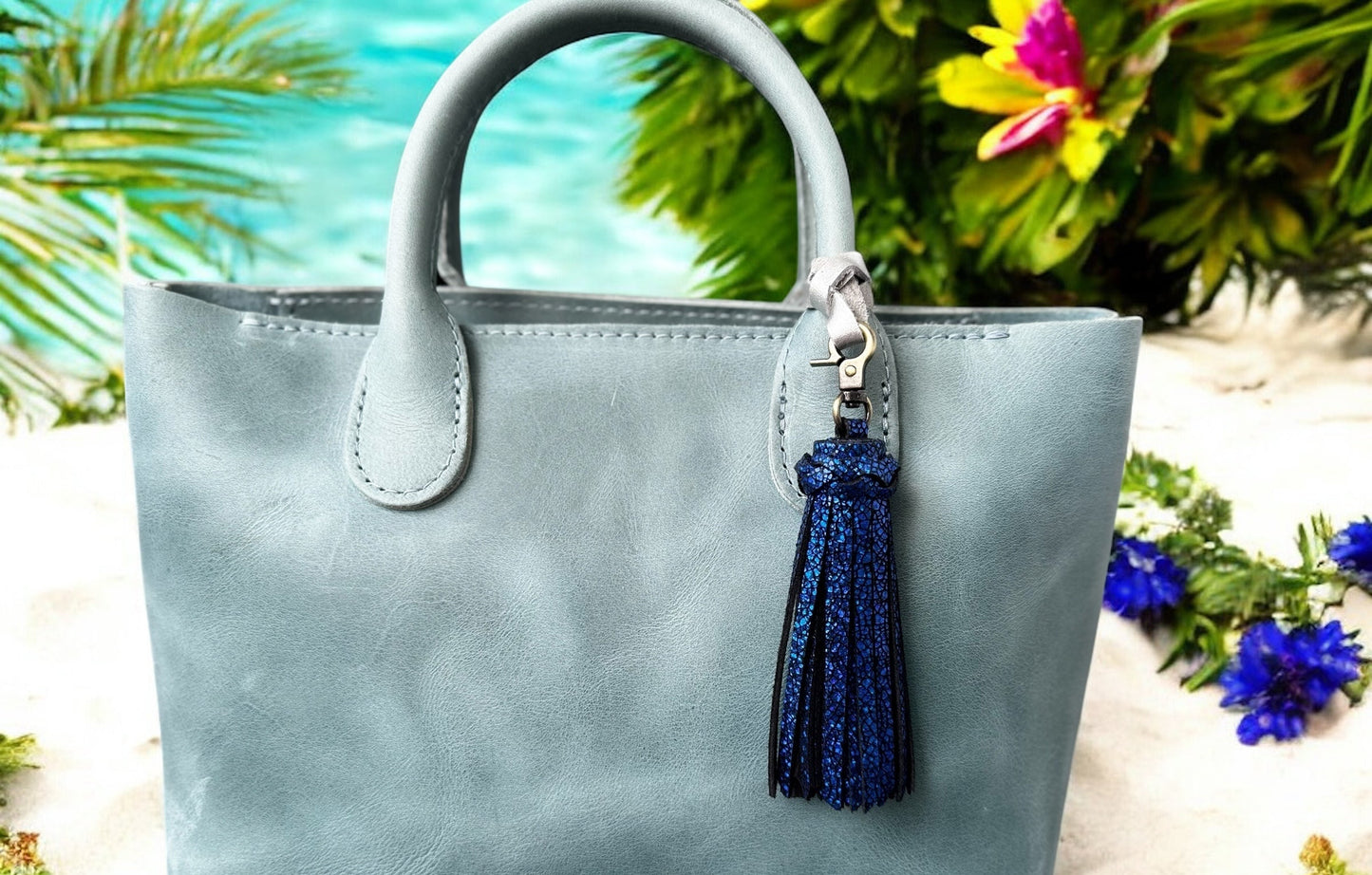 Light blue handbag with a blue tassel keychain against a blurred natural background