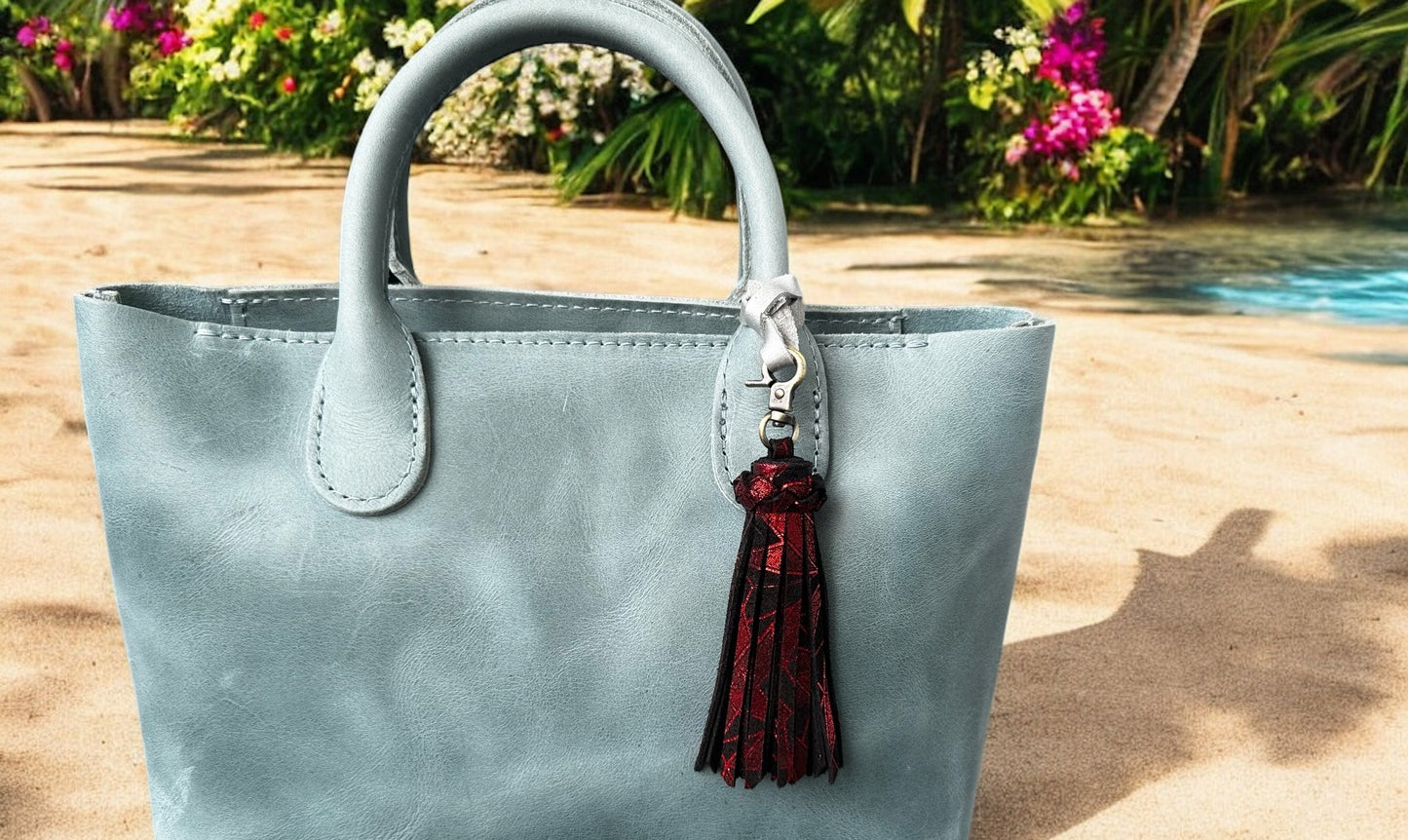 Light blue handbag with a red tassel keychain on a wooden surface with flowers in the background