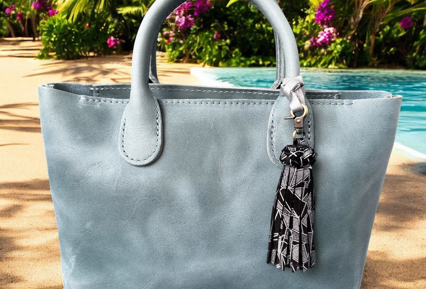 Light blue handbag with a tassel keychain by a poolside