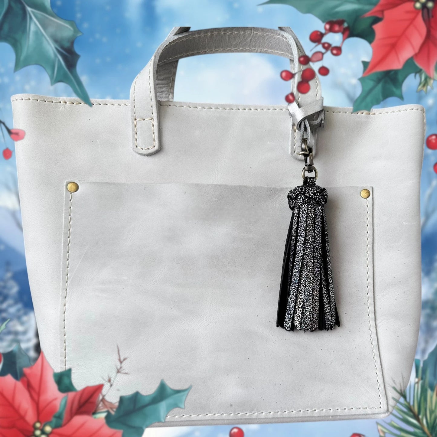 White handbag with a black tassel keychain against a colorful floral background