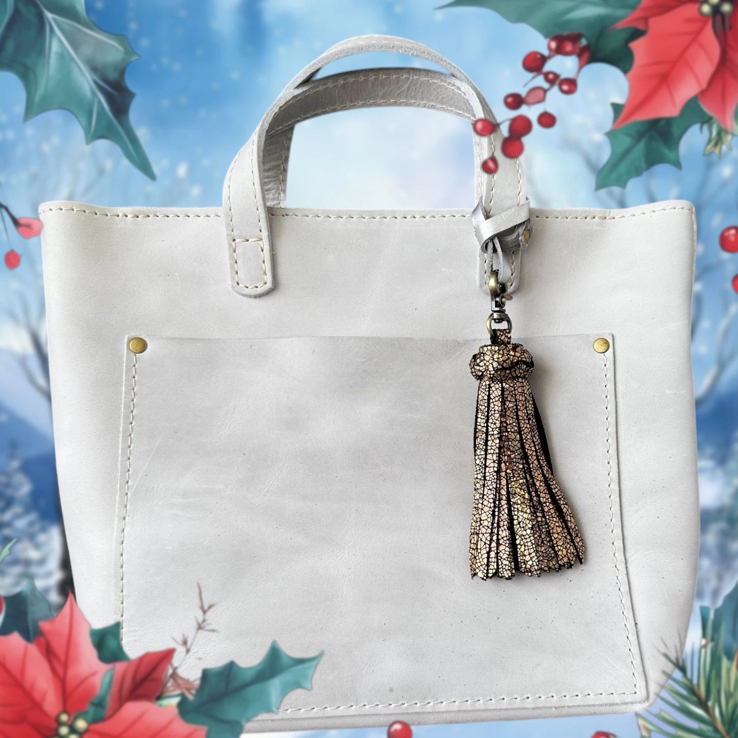 White handbag with a tassel keychain against a festive background with holly leaves and berries.
