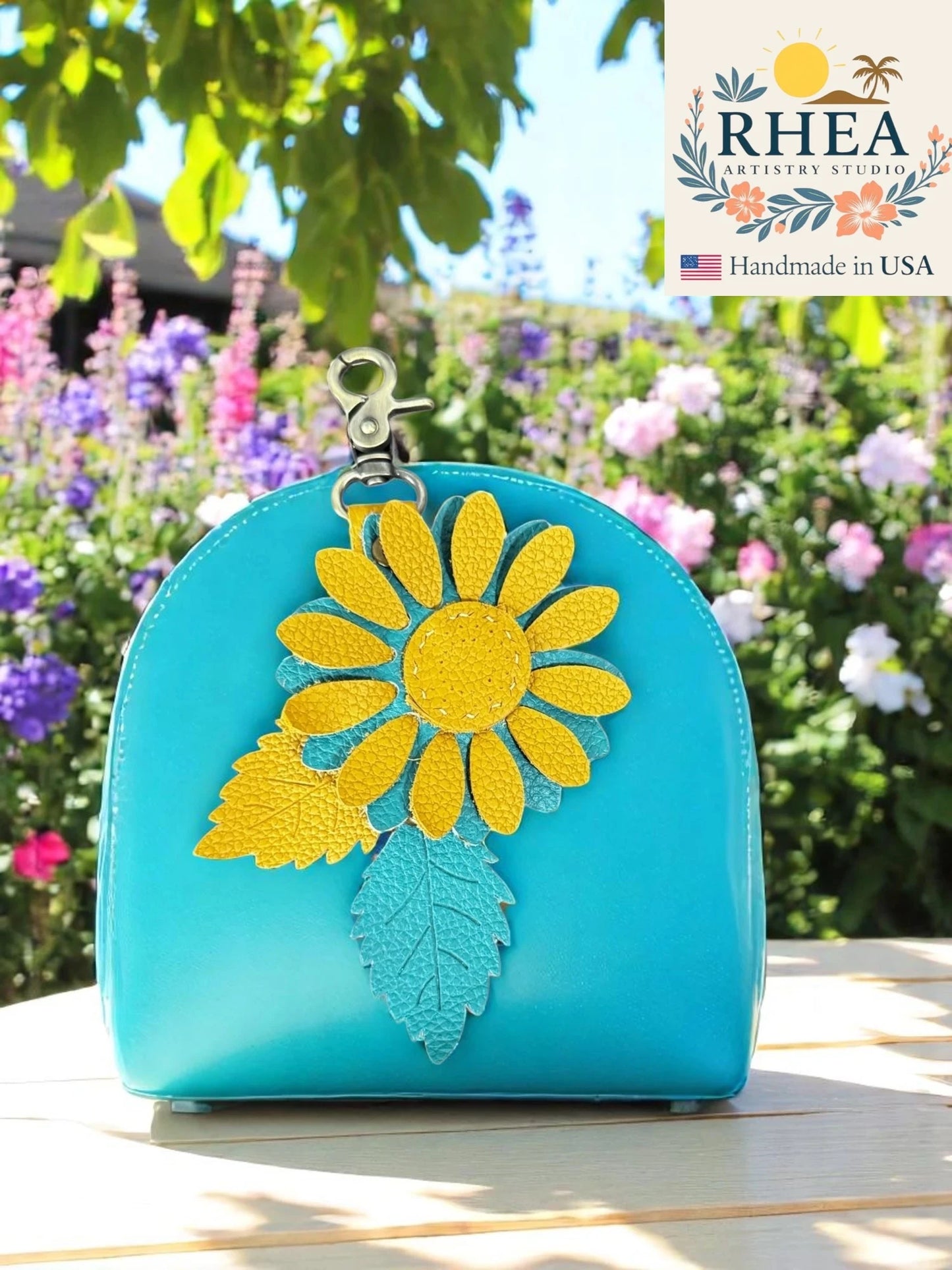 Turquoise handbag with turquoise on a wooden surface with flowers in the background, featuring the RHEEA brand.