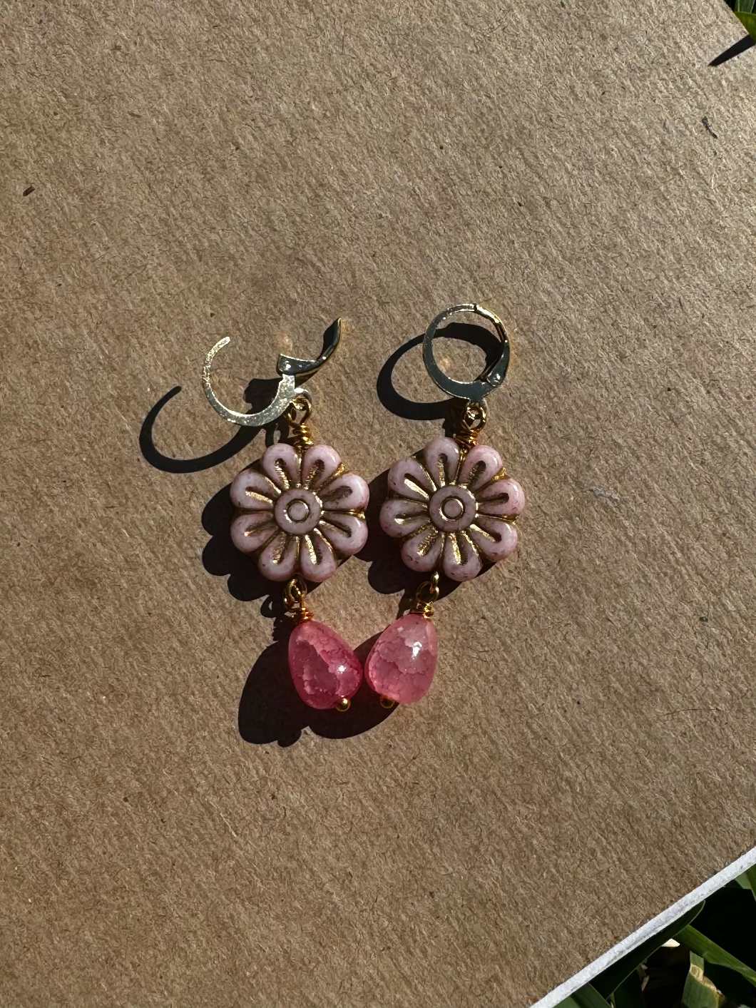 A pair of pale pink daisy-shaped earrings with gold wash and small pink gemstone accents, with gold plated brass findings.