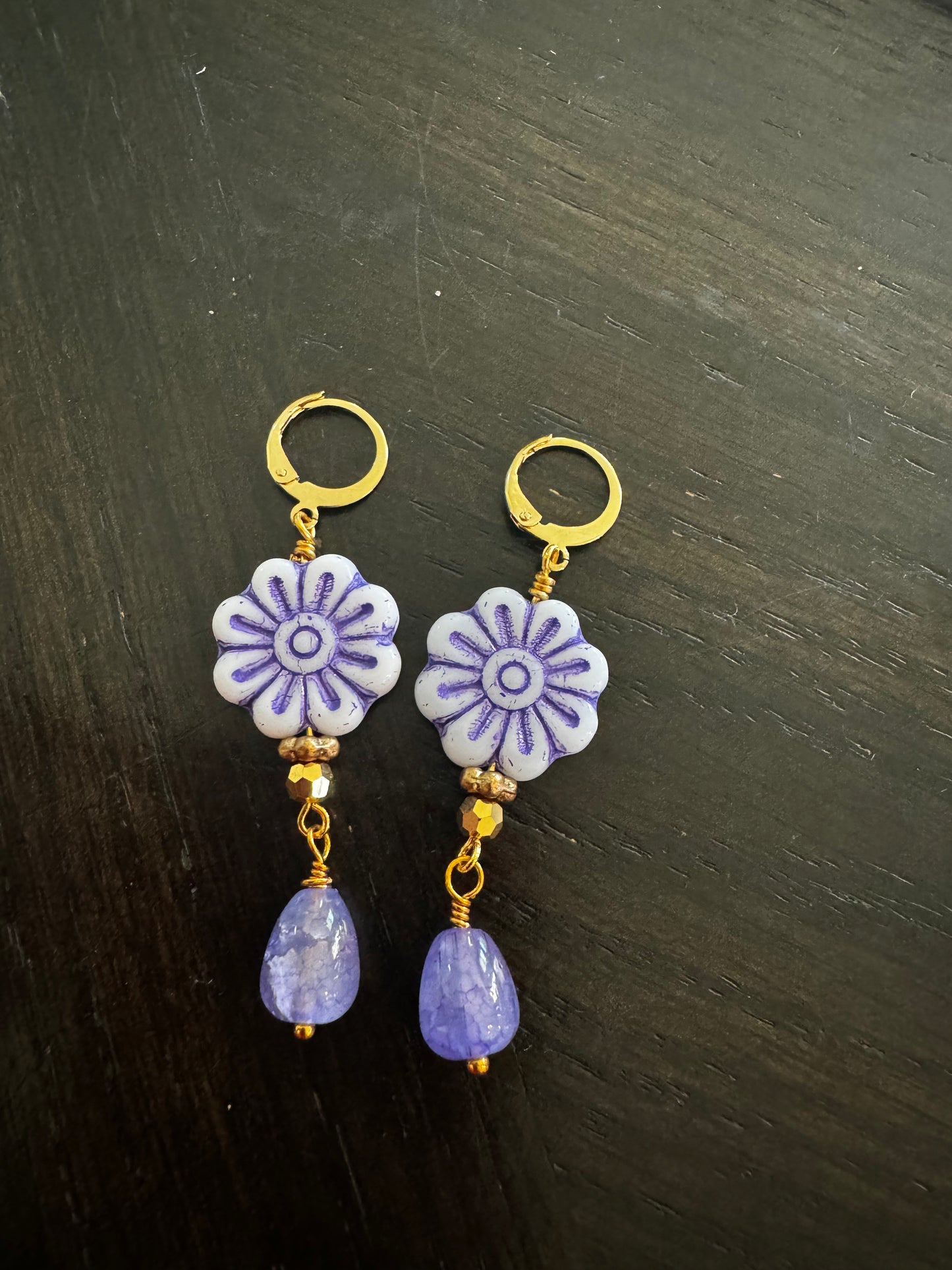 A pair of blue glass drop earrings with gold plated brass findings, displayed on a flat surface with grass and a clear sky in the background.