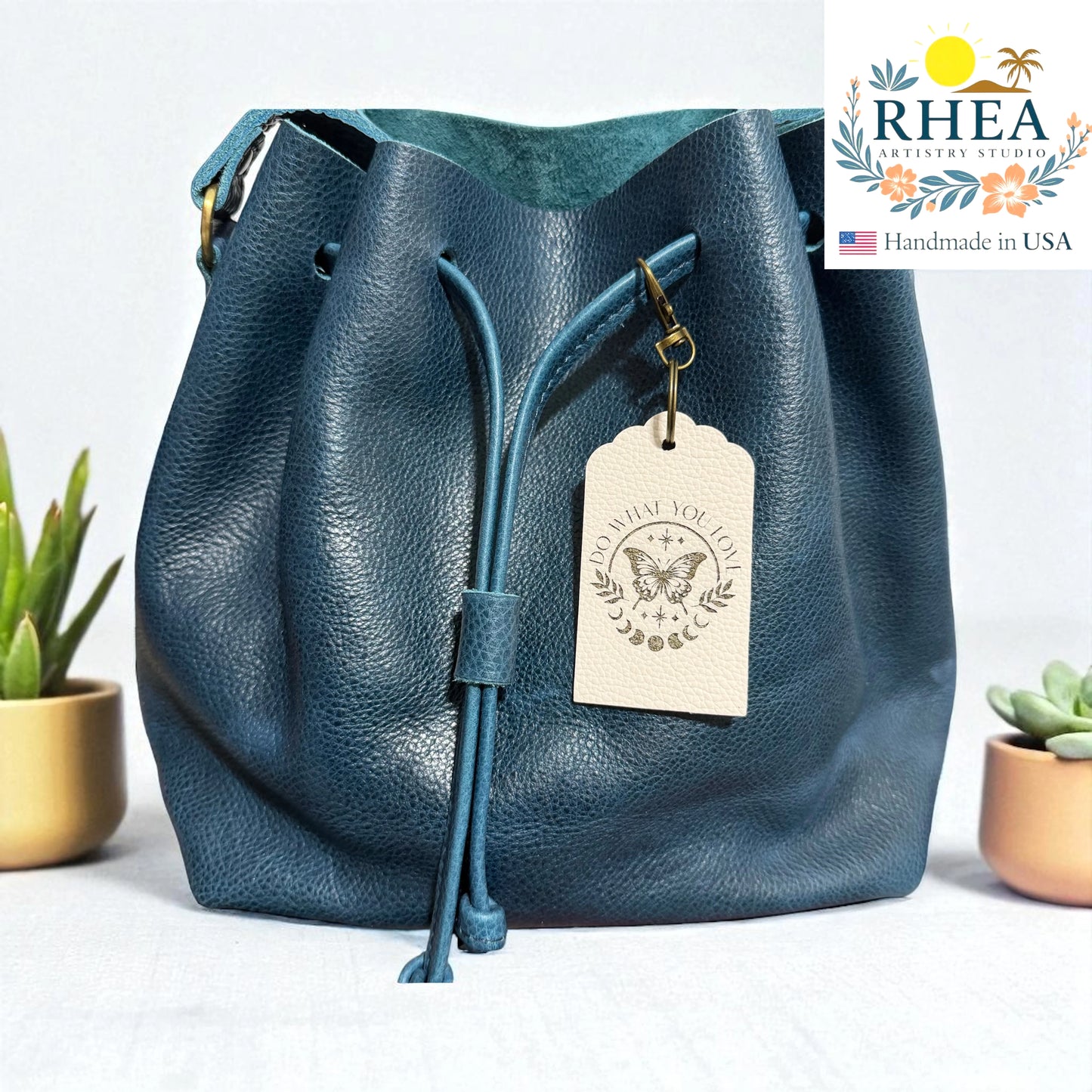 Blue leather bag with a tag on a light background, featuring the RHEA brand.