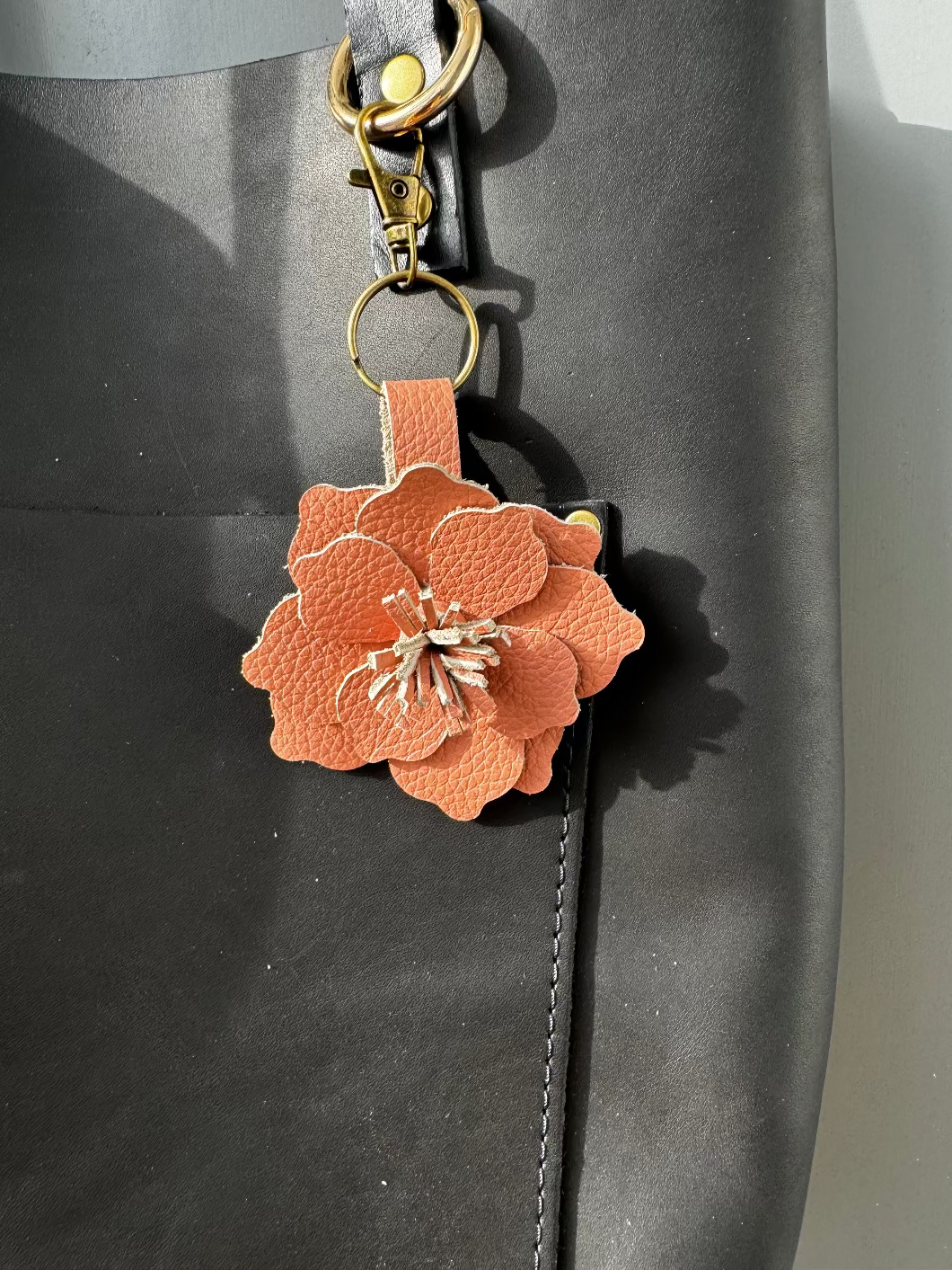 A leather flower accessory in peach fizz color, attached to a lobster clasp and split ring, displayed on a dark textured surface.