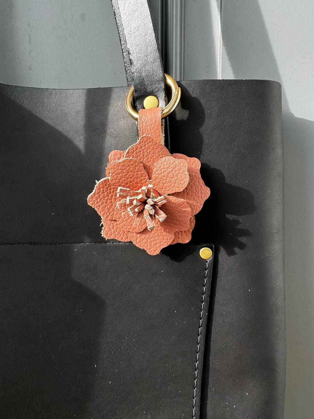 A leather flower accessory in peach fizz color, attached to a lobster clasp and split ring, displayed on a dark textured surface.