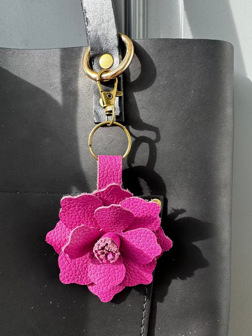A leather flower accessory with a pink and hibiscus flower attached to a black leather strap, featuring a lobster clasp and split ring.