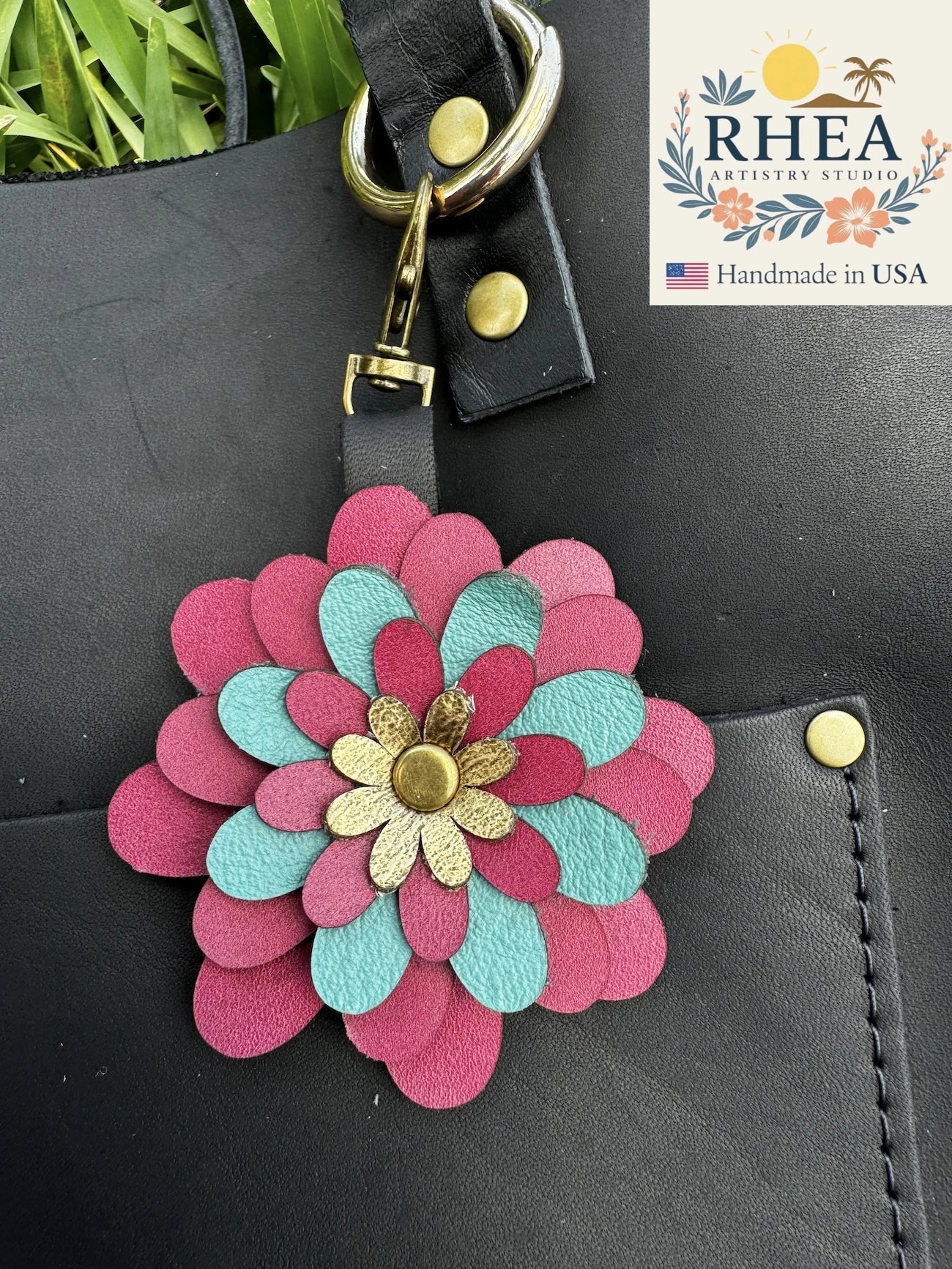 Floral leather purse charm attached to a black bag with RHEA branding.