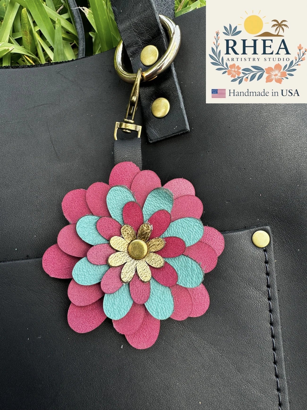 Colorful flower-shaped leather charm attached to a black bag with RHEA Artistry Studio branding.