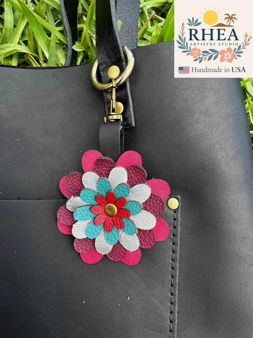 A multi-colored floral design leather purse charm accessory attached to a black bag with a metal clasp.