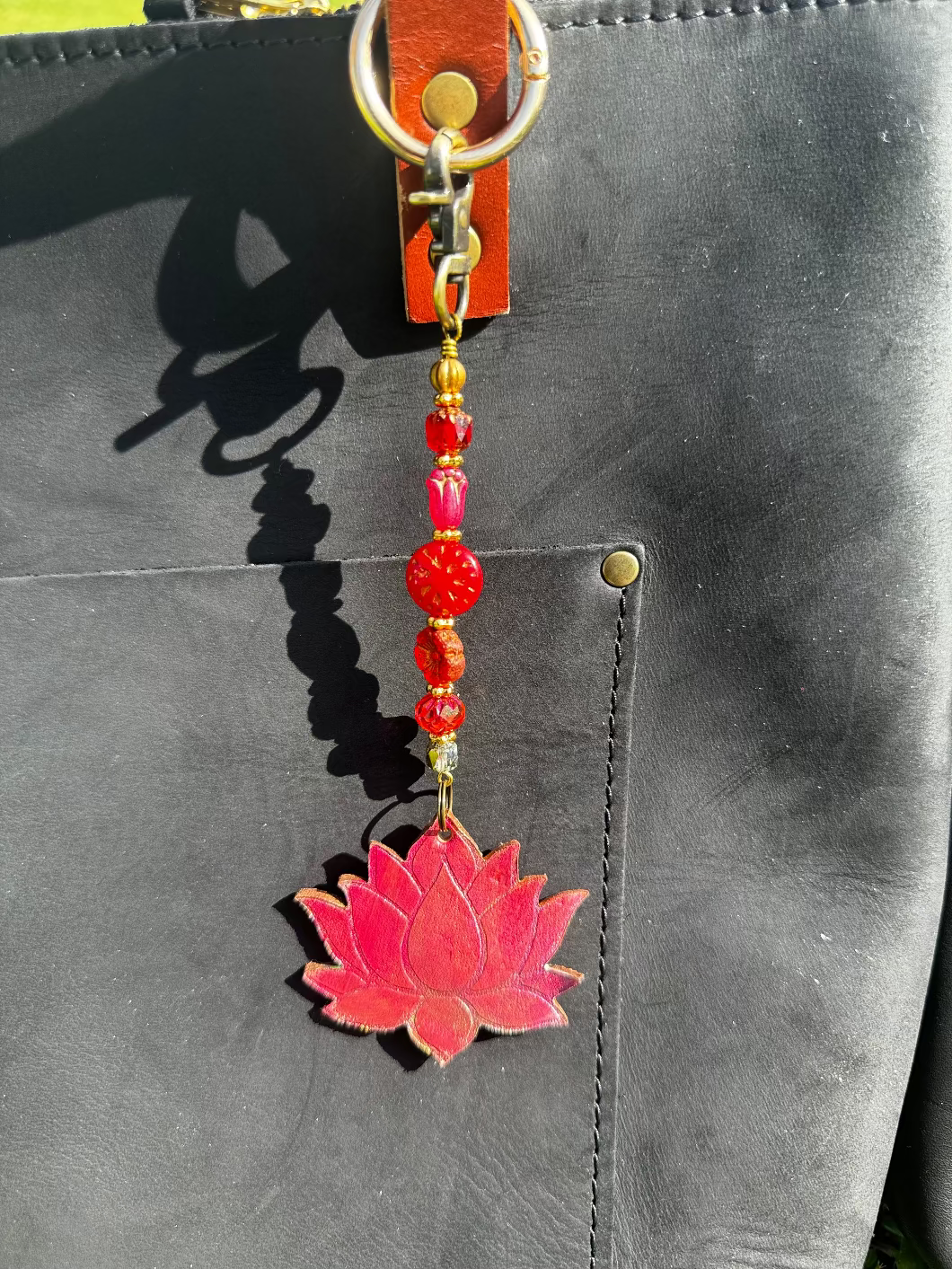 A handcrafted lotus bloom charm made of red and orange glass with brass hardware, attached to a leather-bound notebook.