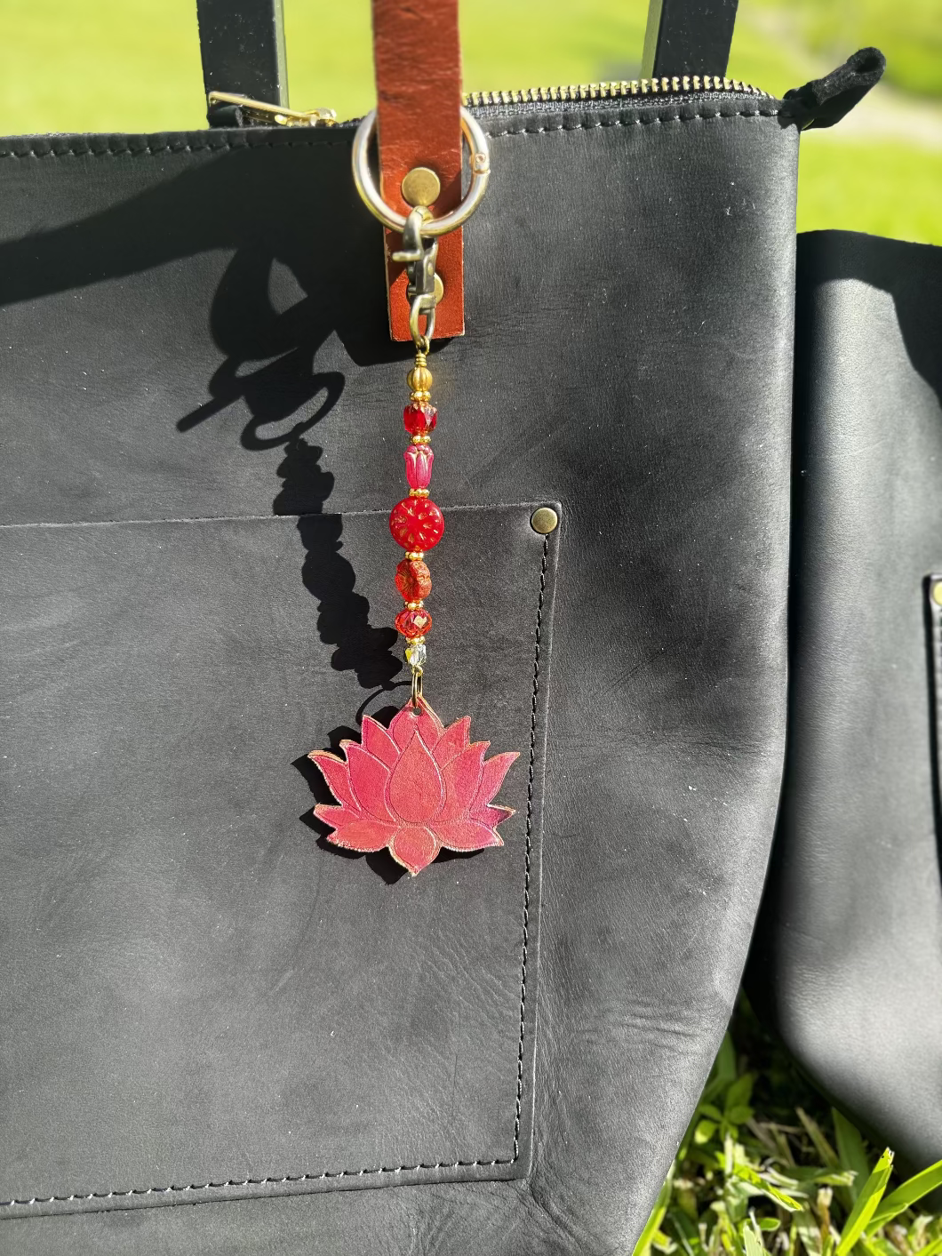 A handcrafted lotus bloom charm made of red and orange glass with brass hardware, attached to a leather-bound notebook.