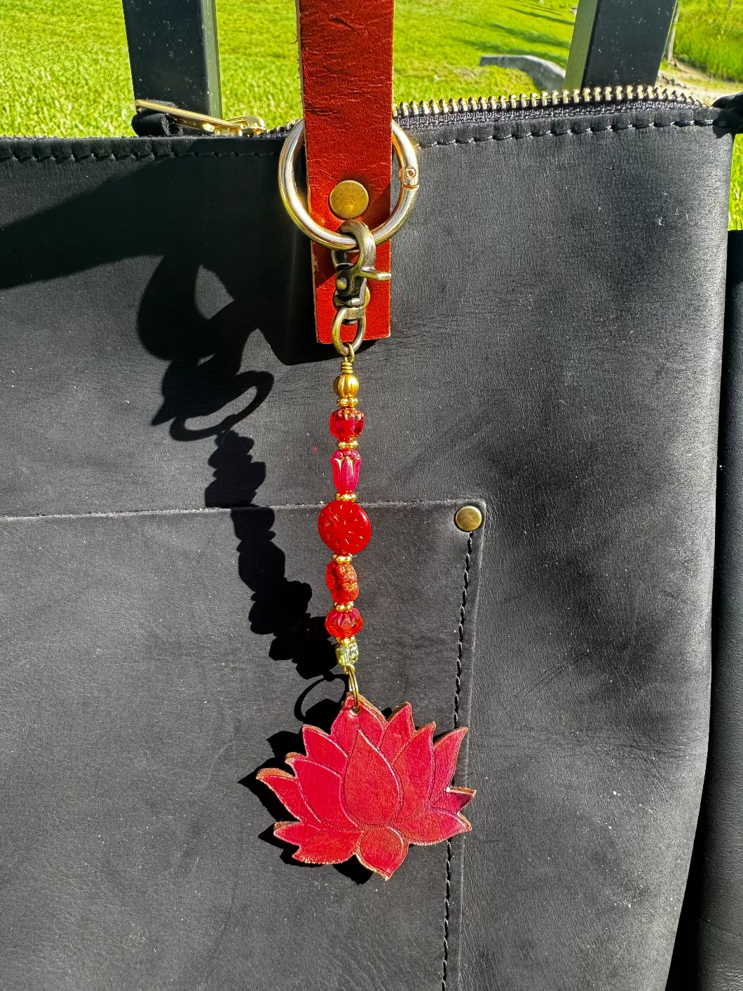 A handcrafted lotus bloom charm made of red and orange glass with brass hardware, attached to a leather-bound notebook.
