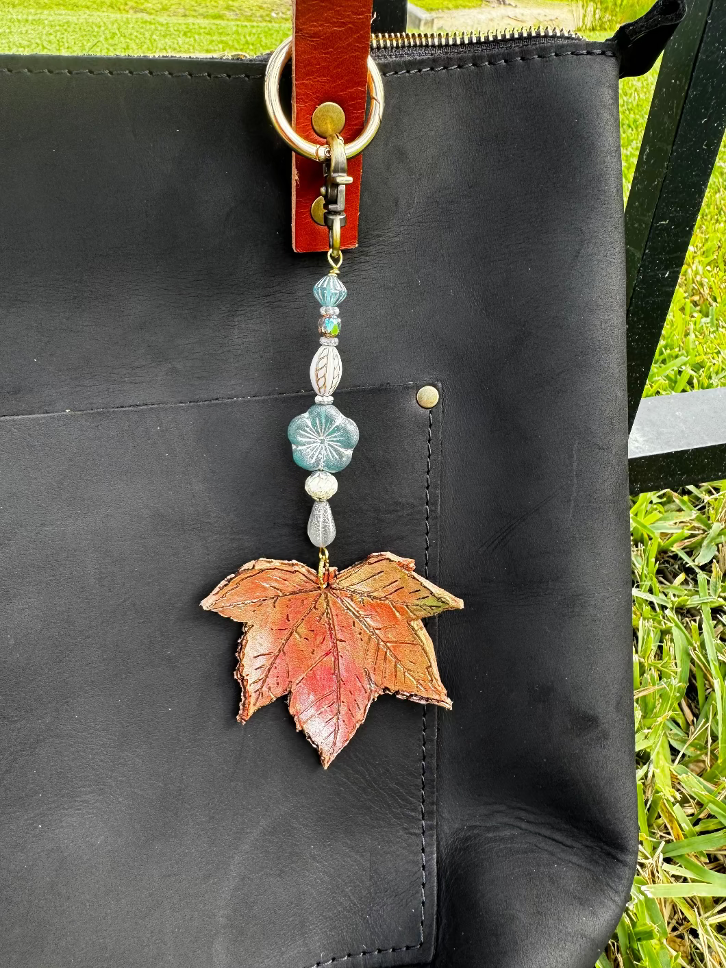 A handcrafted leather charm with a maple/sycamore leaf design, solid brass hardware, and ocean breeze flora, attached to a keychain.