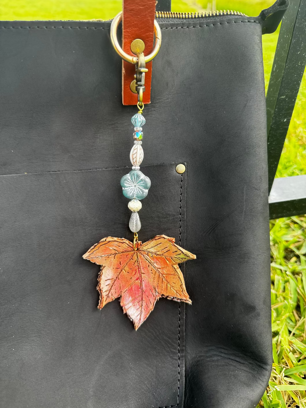 A handcrafted leather charm with a maple/sycamore leaf design, solid brass hardware, and ocean breeze flora, attached to a keychain.