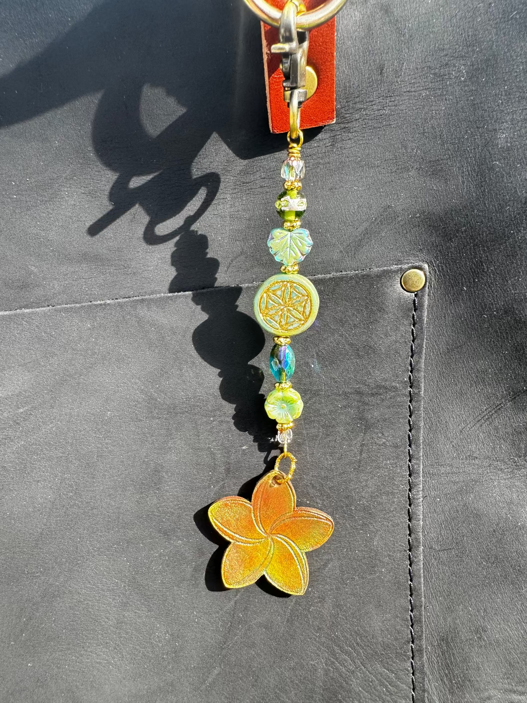 A handcrafted plumeria charm made with leather and solid brass hardware, featuring czech glass accents, attached to a keychain.