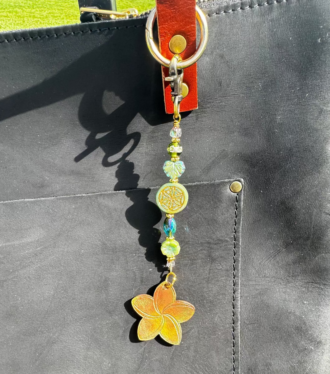 A handcrafted plumeria charm made with leather and solid brass hardware, featuring czech glass accents, attached to a keychain.