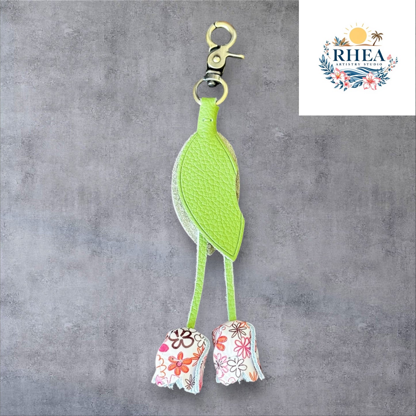 A handmade leather tulip charm with a green leaf and brown floral pattern, attached to a gold lobster clasp on a white marble surface.