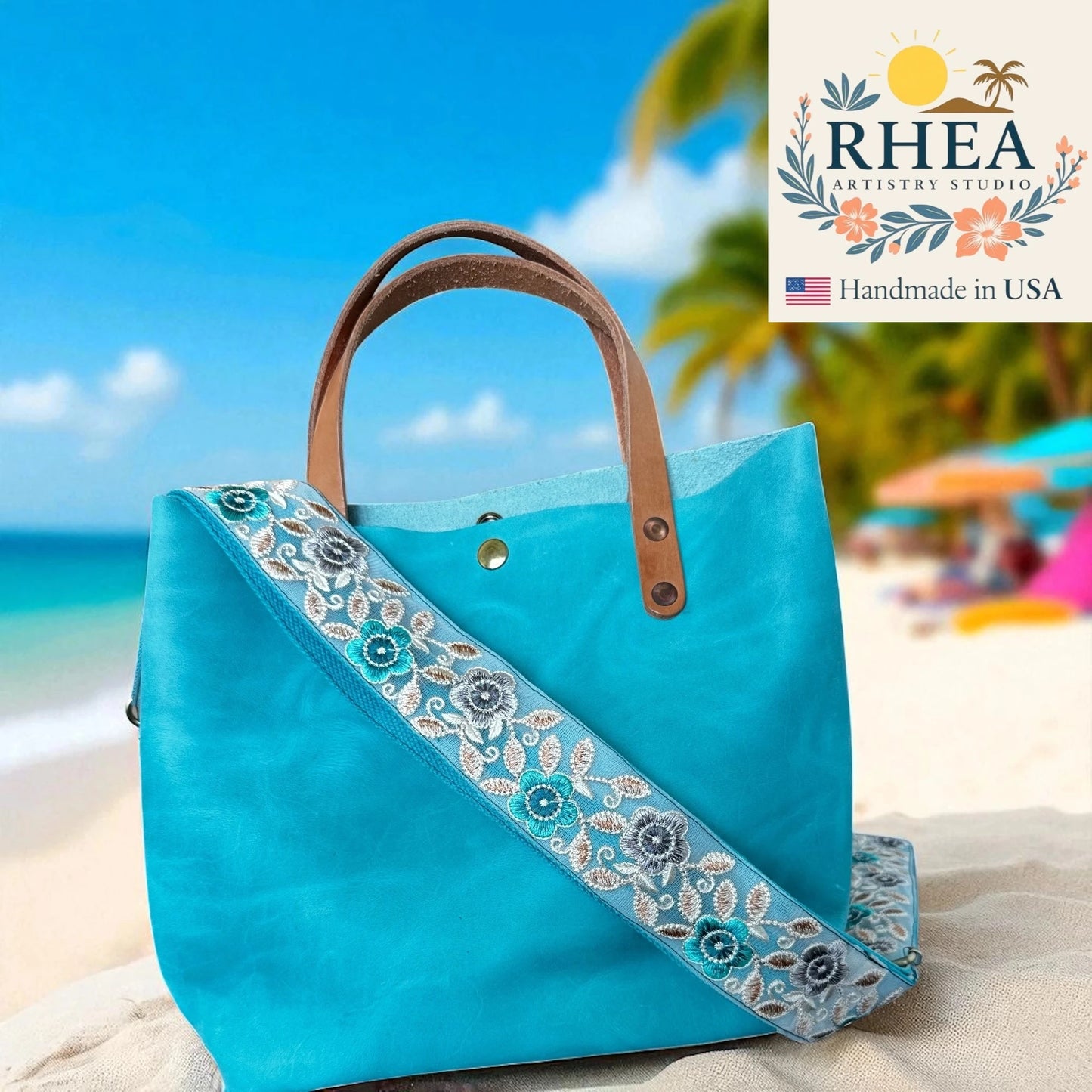 Blue handbag with floral purse strap on a beach, featuring RHEA Artistry Studio logo.