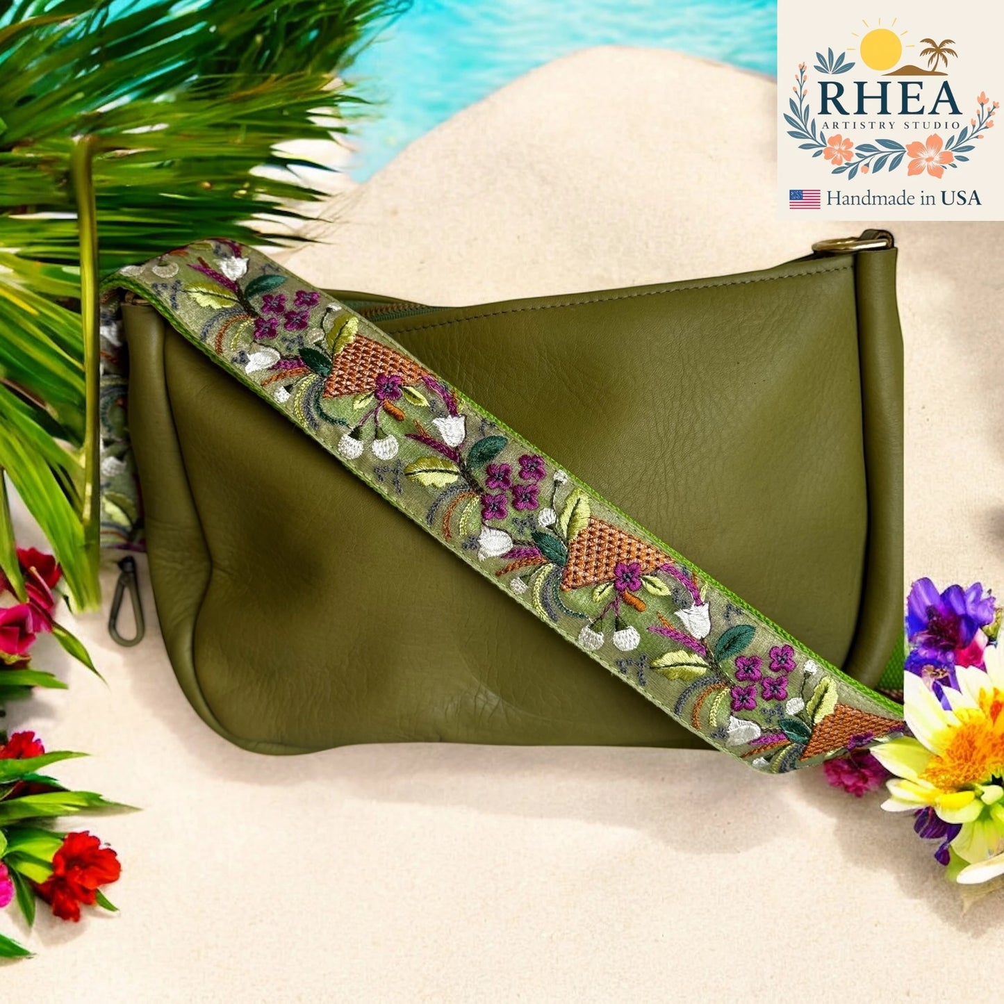 Green clutch bag with floral purse strap on a beach background, featuring the RHEA Artistry Studio logo.