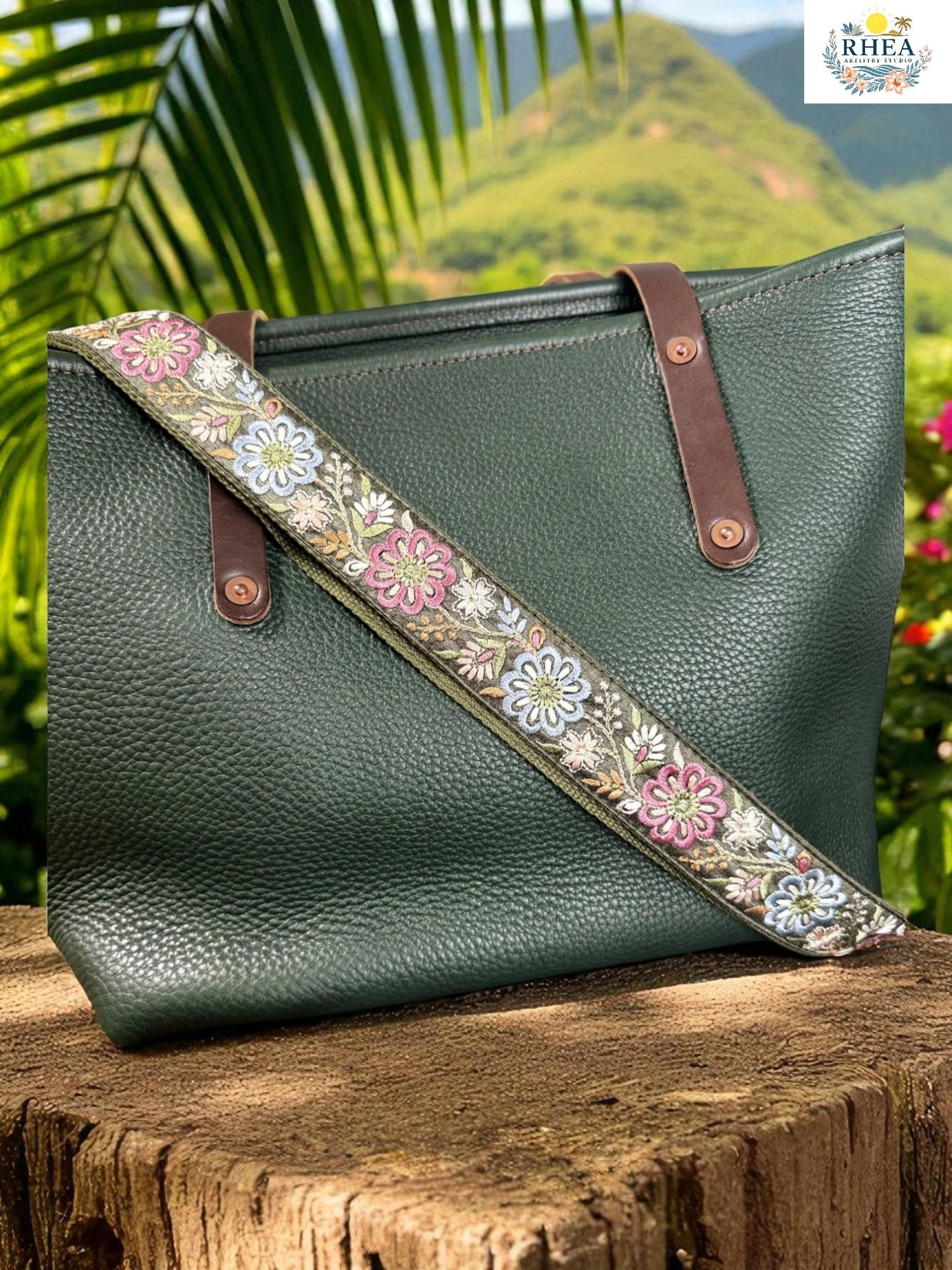 Green leather handbag with a floral strap on a wooden surface with a natural background