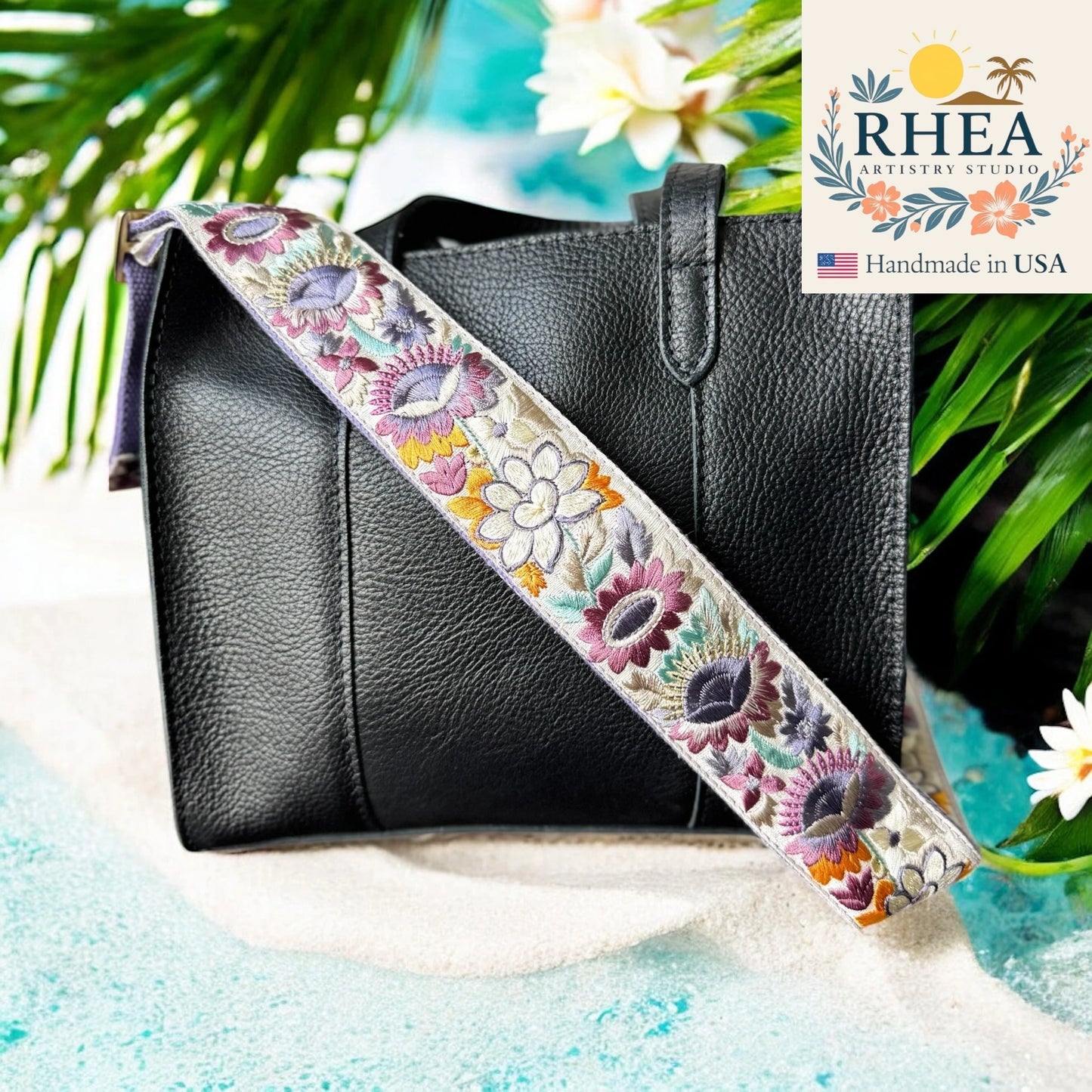 Black handbag with a floral purse strap against a natural background, featuring the RHEA Artistry Studios logo.