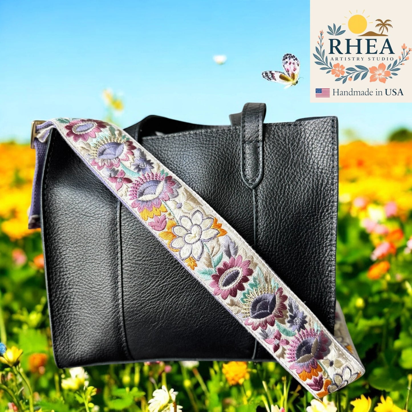 Black handbag with a floral embroidered purse strap against a colorful outdoor background, featuring the RHEA Artistry Studio logo.
