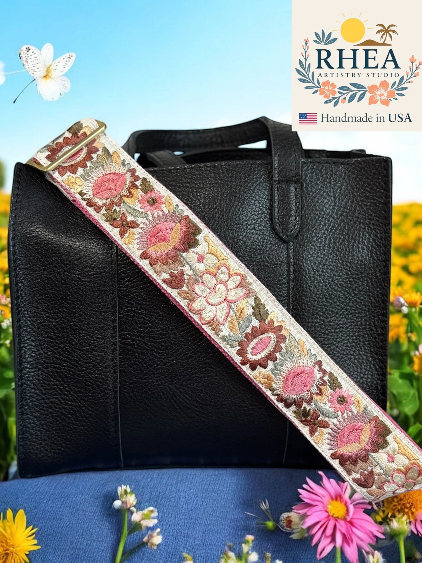 Black handbag with a floral purse strap against a natural background, featuring the RHEA Artisan Studio logo.