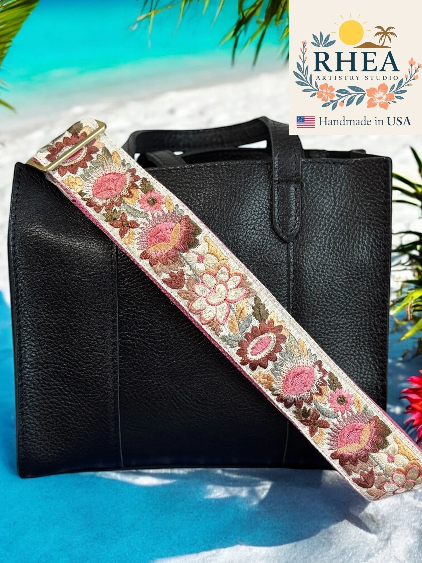 Black leather bag with a floral purse strap on a beach background, featuring the RHEEA brand.